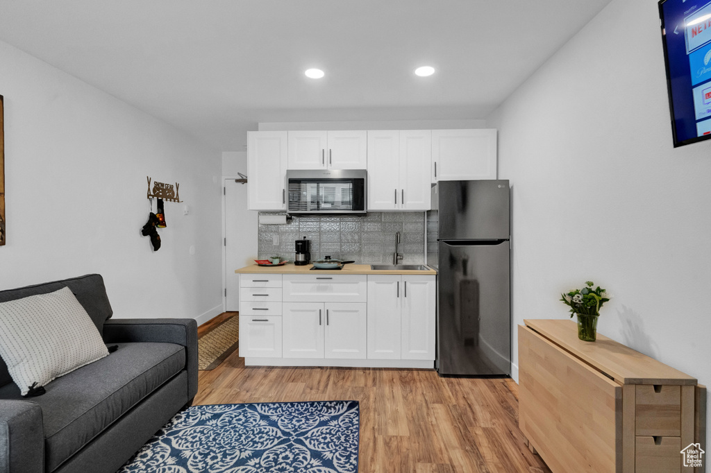 Kitchen featuring black refrigerator, light hardwood / wood-style flooring, white cabinetry, backsplash, and sink