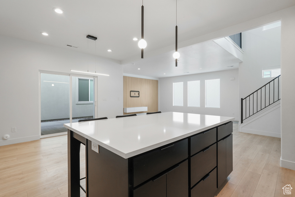Kitchen with decorative light fixtures, light hardwood / wood-style flooring, a healthy amount of sunlight, and a kitchen island