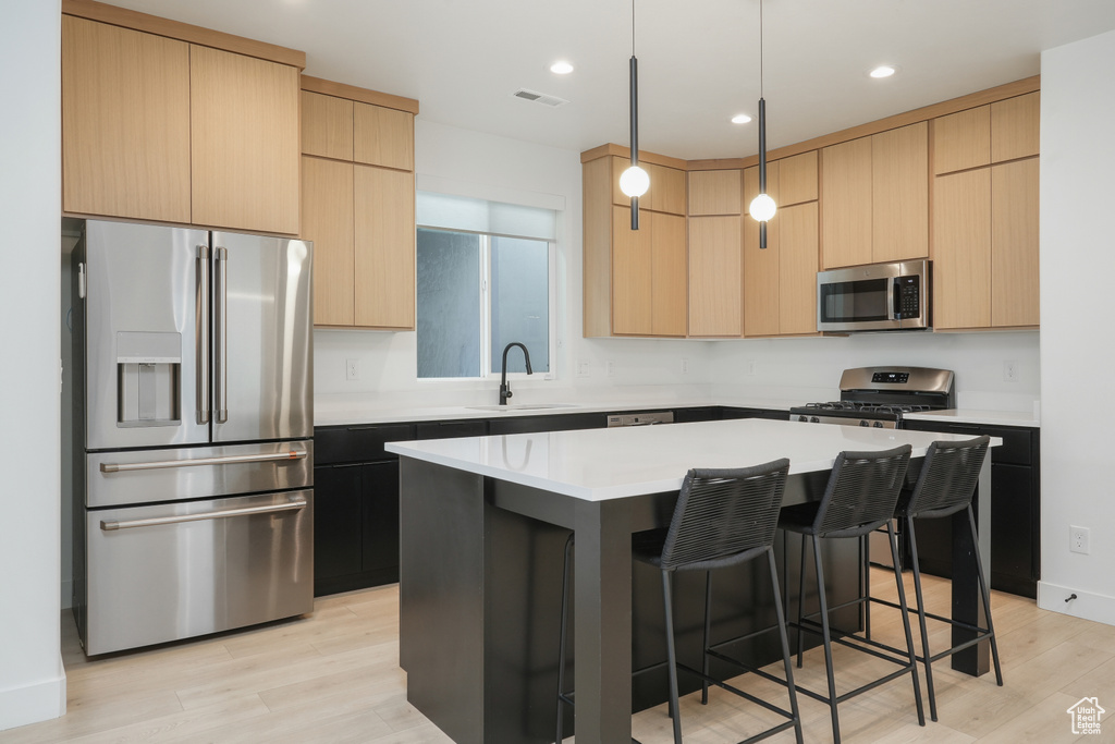 Kitchen with a center island, pendant lighting, appliances with stainless steel finishes, sink, and light hardwood / wood-style floors