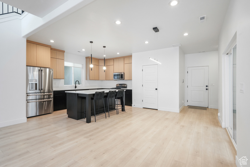 Kitchen featuring a kitchen island, hanging light fixtures, a breakfast bar area, stainless steel appliances, and light hardwood / wood-style floors