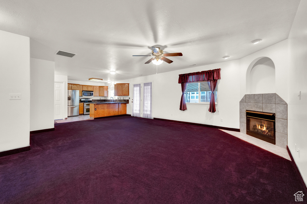 Unfurnished living room featuring ceiling fan, sink, dark carpet, and a tiled fireplace