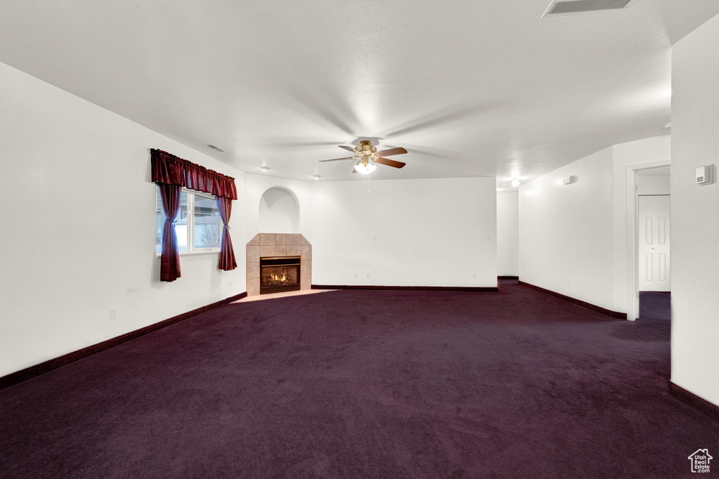 Empty room featuring dark colored carpet, ceiling fan, and a tiled fireplace