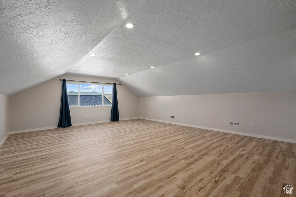 Additional living space featuring light hardwood / wood-style floors, a textured ceiling, and lofted ceiling