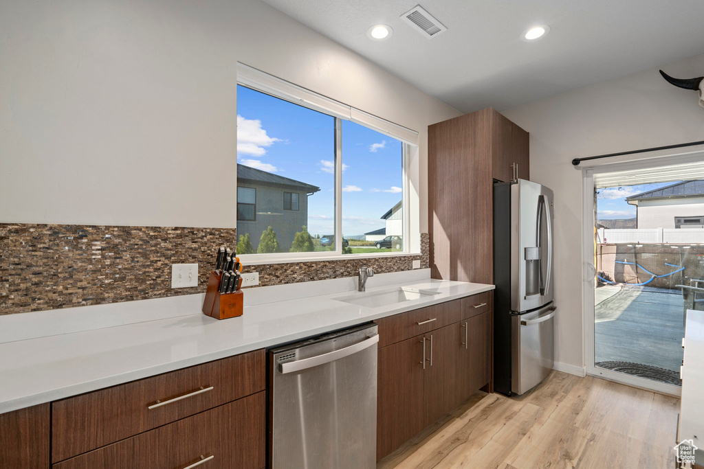 Kitchen with dark brown cabinets, appliances with stainless steel finishes, backsplash, sink, and light wood-type flooring