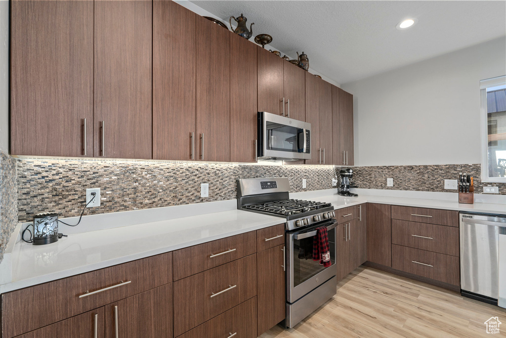Kitchen featuring backsplash, dark brown cabinets, light hardwood / wood-style floors, and stainless steel appliances