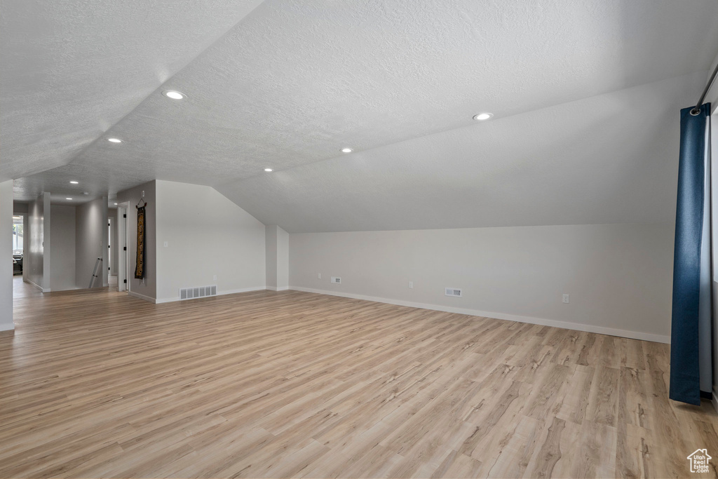 Bonus room with vaulted ceiling, light hardwood / wood-style floors, and a textured ceiling