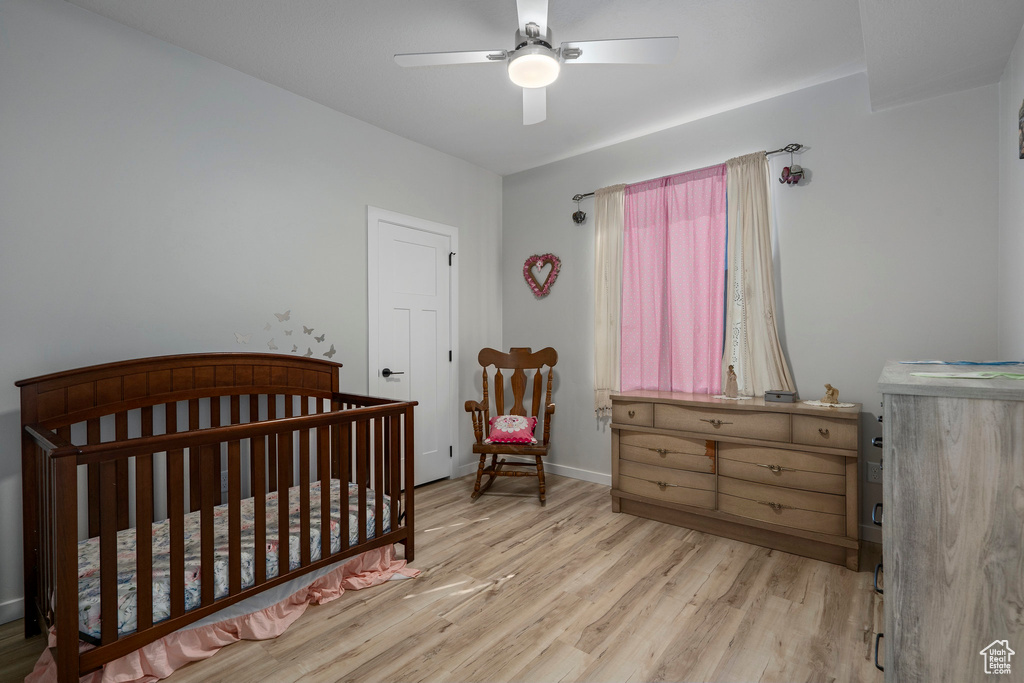 Bedroom with ceiling fan, light hardwood / wood-style floors, and a nursery area