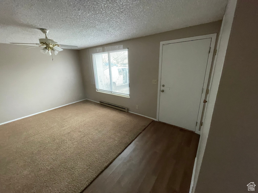 Unfurnished room with hardwood / wood-style flooring, a baseboard heating unit, ceiling fan, and a textured ceiling