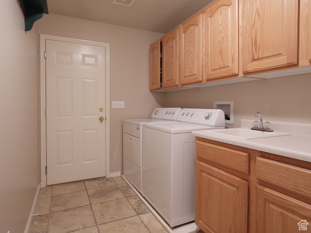 Washroom with hookup for a washing machine, cabinets, washing machine and clothes dryer, sink, and light tile floors