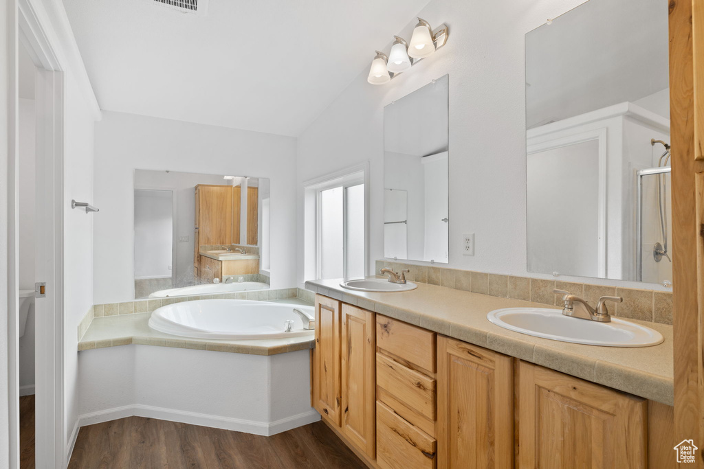 Bathroom featuring vanity with extensive cabinet space, hardwood / wood-style floors, a washtub, dual sinks, and lofted ceiling