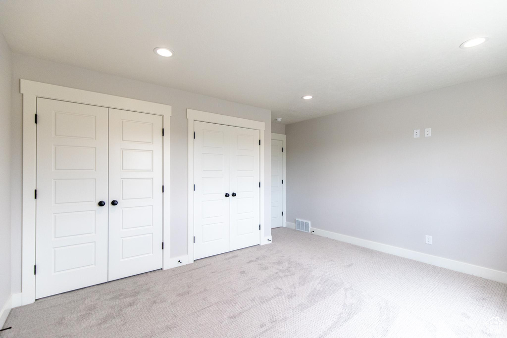 Unfurnished bedroom featuring light colored carpet and multiple closets