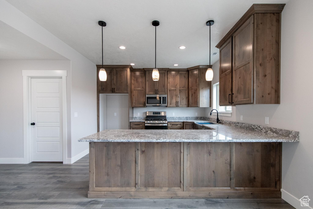 Kitchen with pendant lighting, dark wood-type flooring, kitchen peninsula, stainless steel appliances, and sink