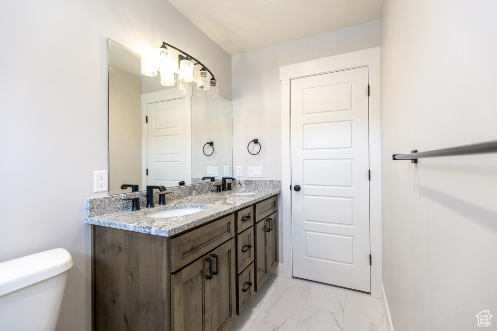 Bathroom featuring tile floors, vanity with extensive cabinet space, toilet, and double sink
