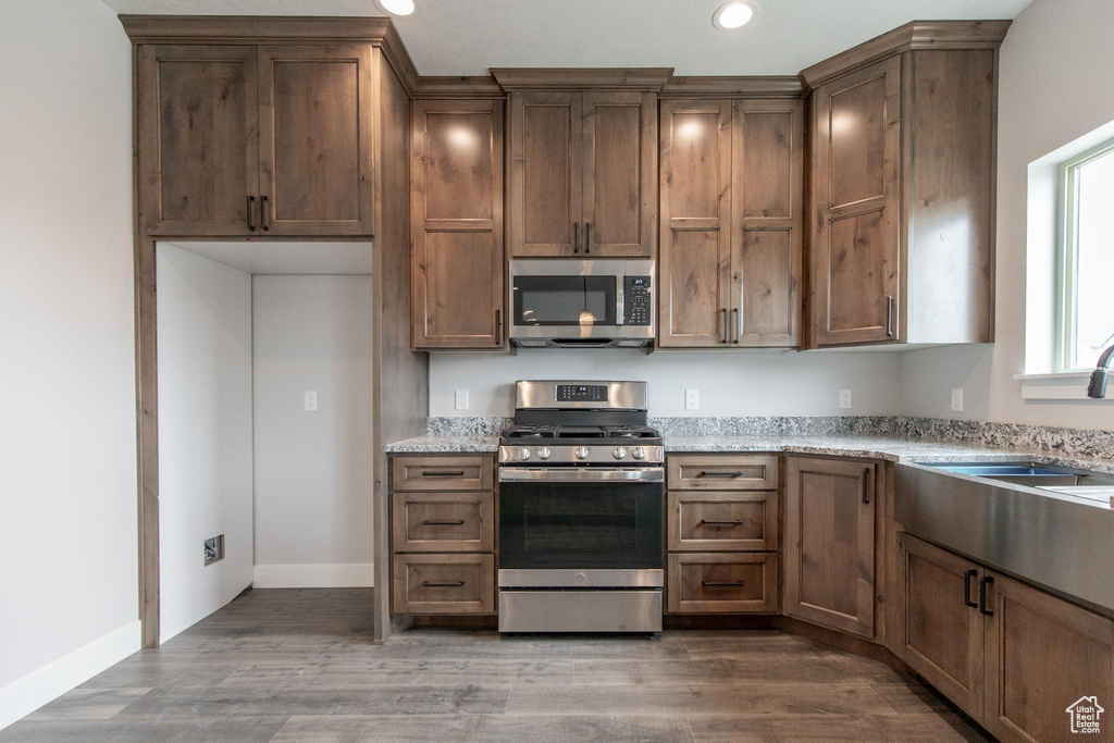 Kitchen featuring wood-type flooring, appliances with stainless steel finishes, sink, and light stone countertops