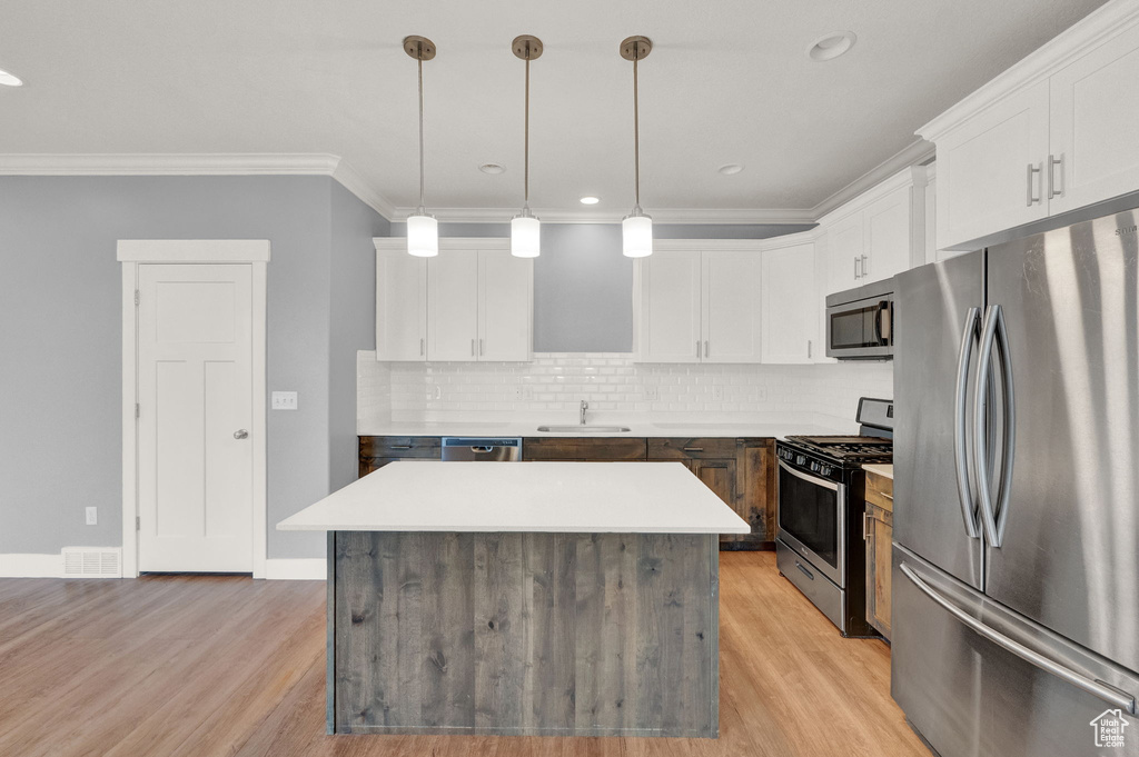 Kitchen with white cabinets, a kitchen island, stainless steel appliances, and light hardwood / wood-style floors