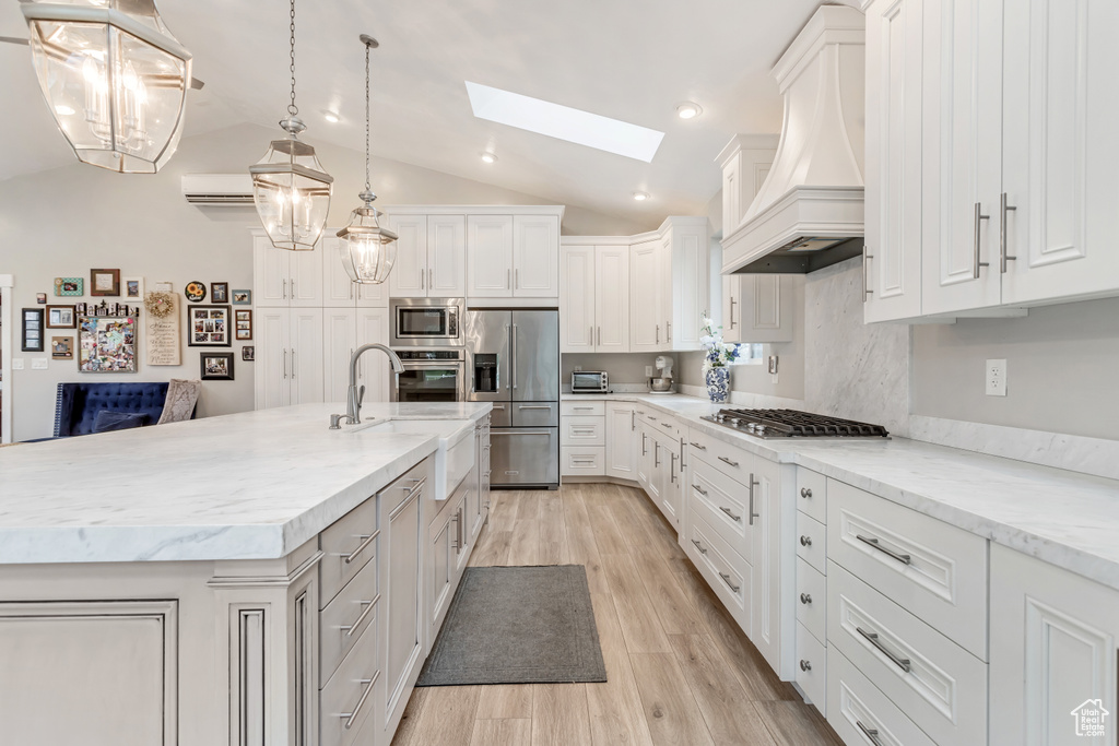 Kitchen with hanging light fixtures, light wood-type flooring, white cabinetry, custom range hood, and appliances with stainless steel finishes