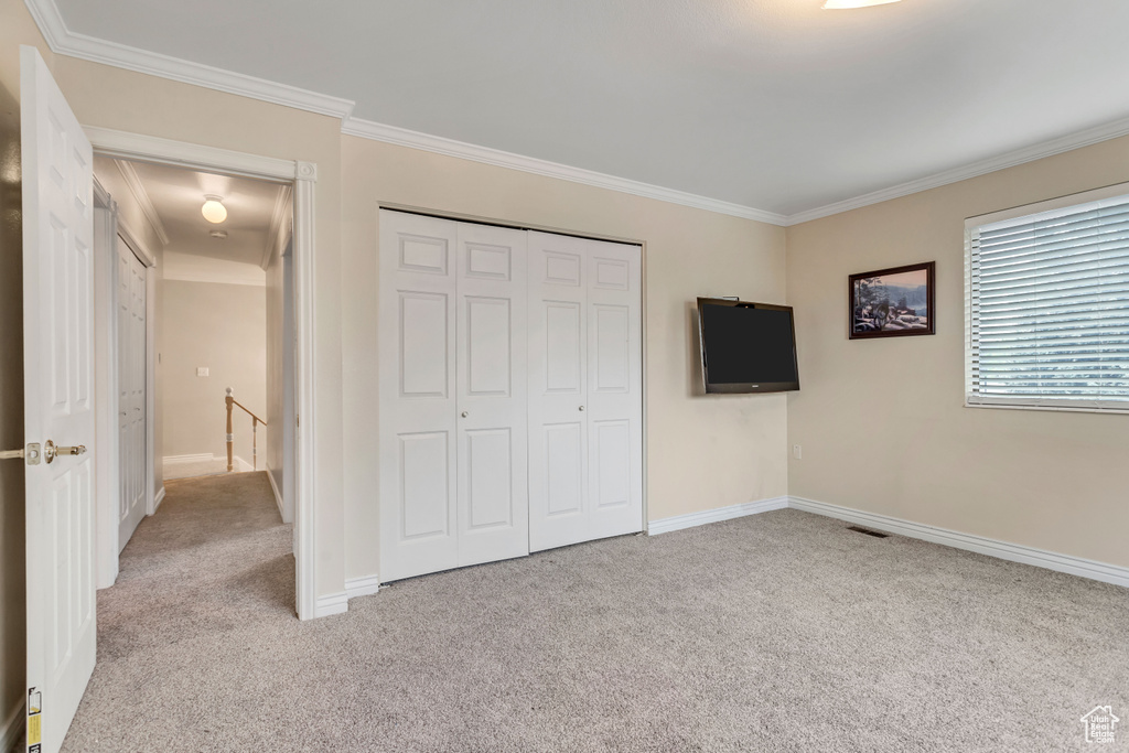 Unfurnished bedroom with ornamental molding, light carpet, and a closet