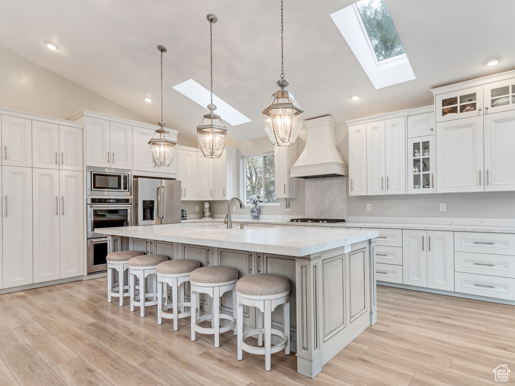 Kitchen with stainless steel appliances, custom range hood, a skylight, pendant lighting, and light wood-type flooring