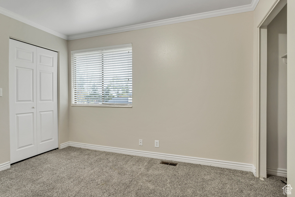 Unfurnished bedroom featuring light colored carpet, a closet, and crown molding