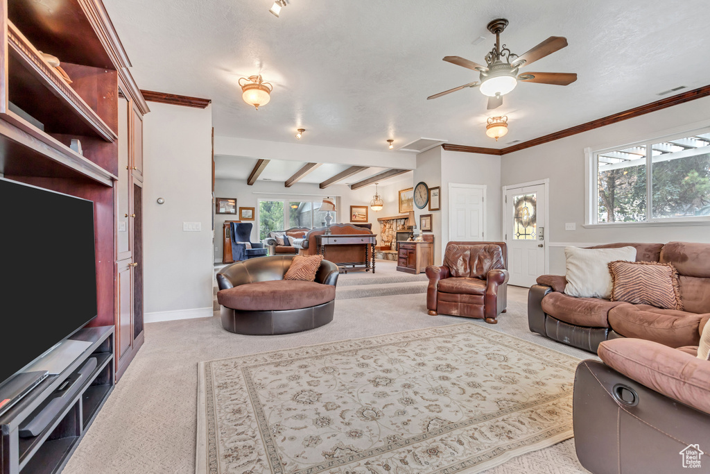 Carpeted living room featuring crown molding, ceiling fan, and beamed ceiling