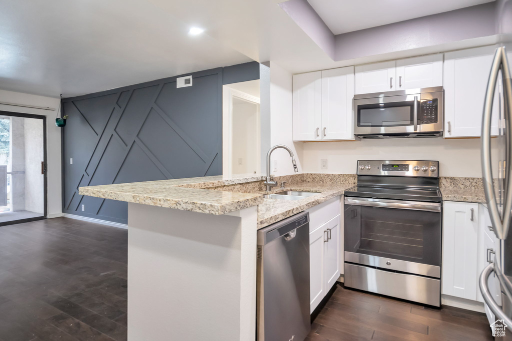 Kitchen featuring appliances with stainless steel finishes, dark hardwood / wood-style floors, light stone counters, white cabinets, and sink