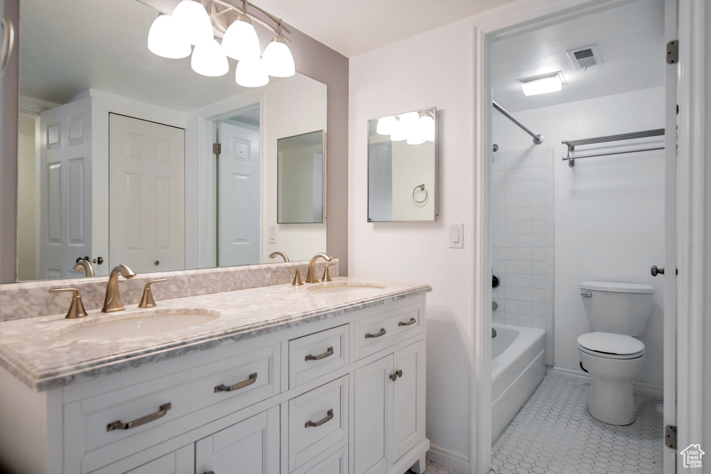 Full bathroom with tiled shower / bath, oversized vanity, tile flooring, dual sinks, and toilet