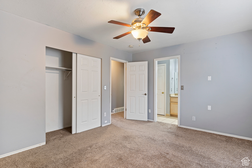 Unfurnished bedroom with a closet, ceiling fan, light tile floors, and ensuite bathroom
