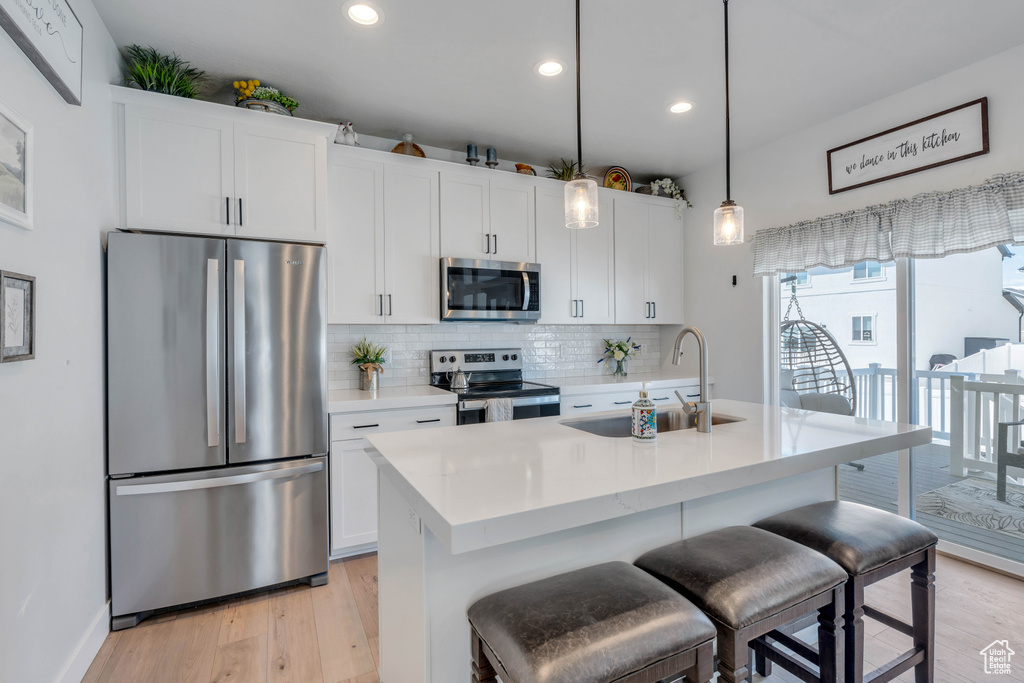 Kitchen featuring stainless steel appliances, a center island with sink, white cabinetry, sink, and pendant lighting