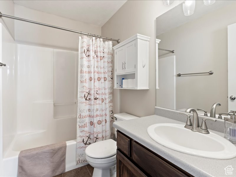 Full bathroom with shower / bath combo, vanity with extensive cabinet space, toilet, and tile flooring