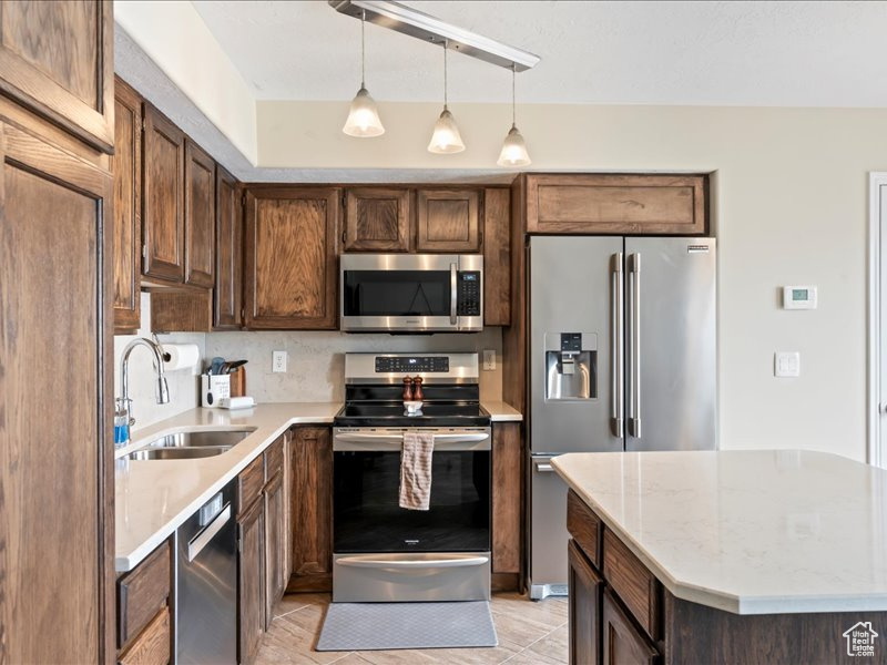 Kitchen with decorative light fixtures, appliances with stainless steel finishes, light tile flooring, light stone counters, and sink
