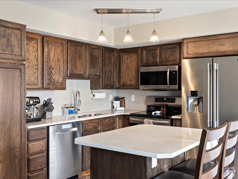 Kitchen featuring pendant lighting, stainless steel appliances, sink, a kitchen bar, and tasteful backsplash