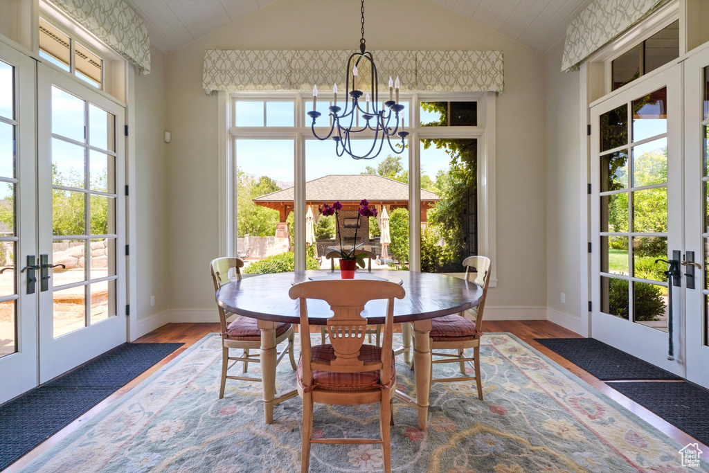 Dining space featuring vaulted ceiling, light hardwood / wood-style flooring, a chandelier, and french doors