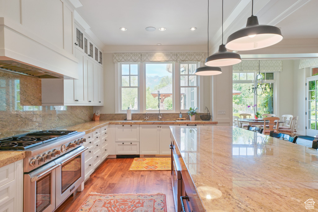Kitchen with custom range hood, light hardwood / wood-style floors, white cabinets, and range with gas cooktop