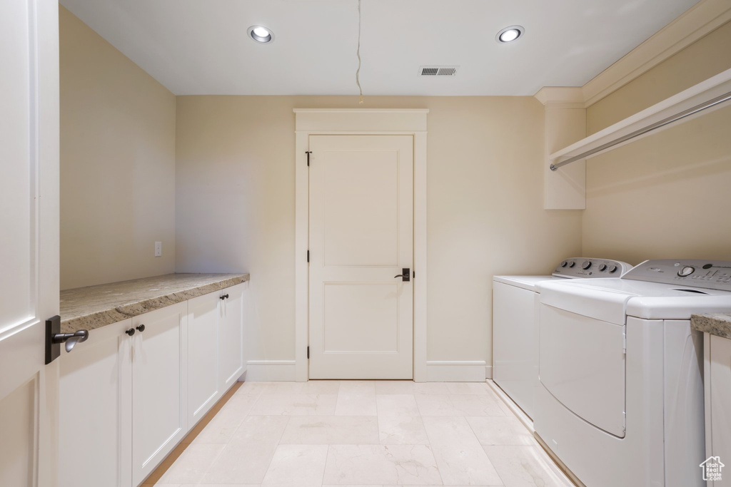Clothes washing area with cabinets, washing machine and dryer, and light tile flooring