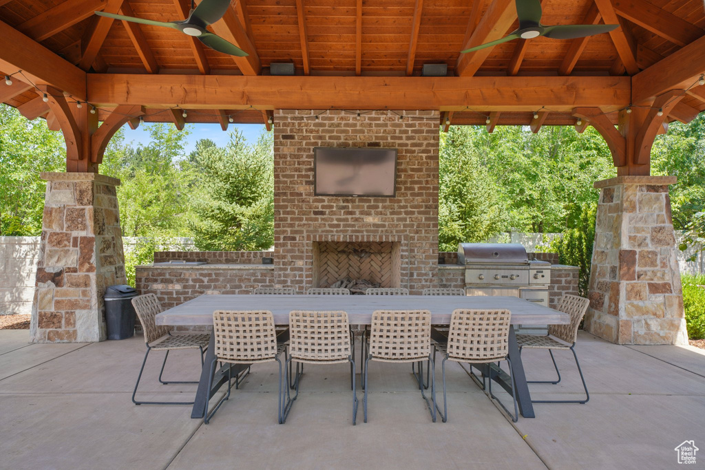 View of terrace with an outdoor brick fireplace, ceiling fan, a gazebo, and grilling area