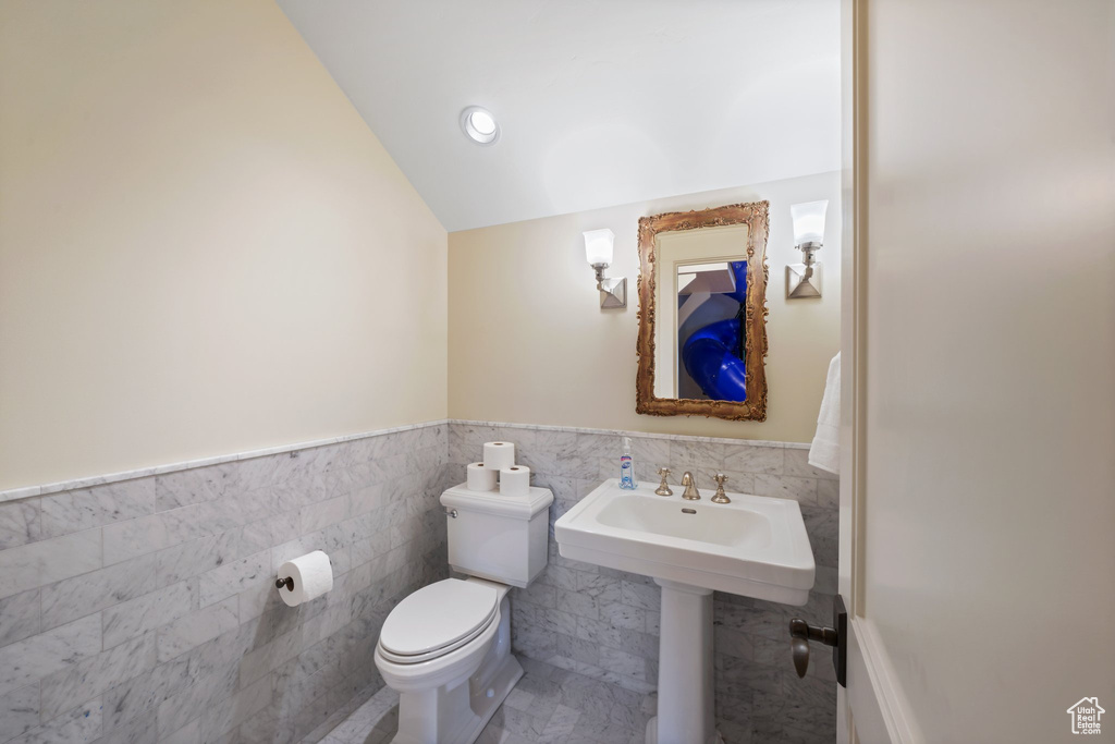 Bathroom featuring toilet, tile flooring, tile walls, and lofted ceiling
