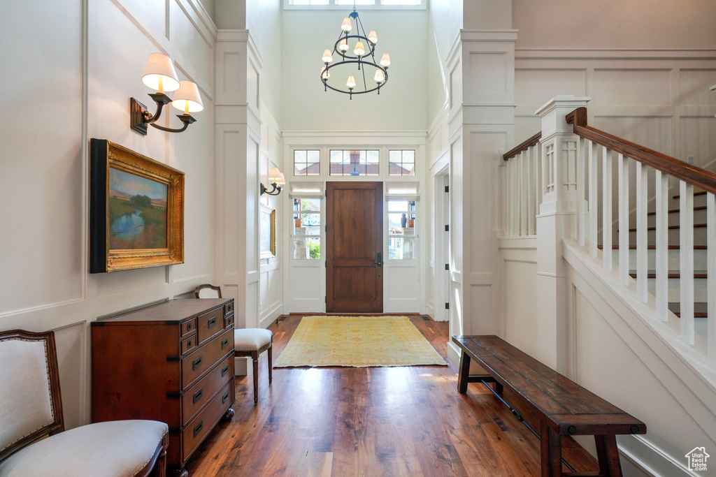 Entryway featuring wood-type flooring, ornate columns, a towering ceiling, and an inviting chandelier