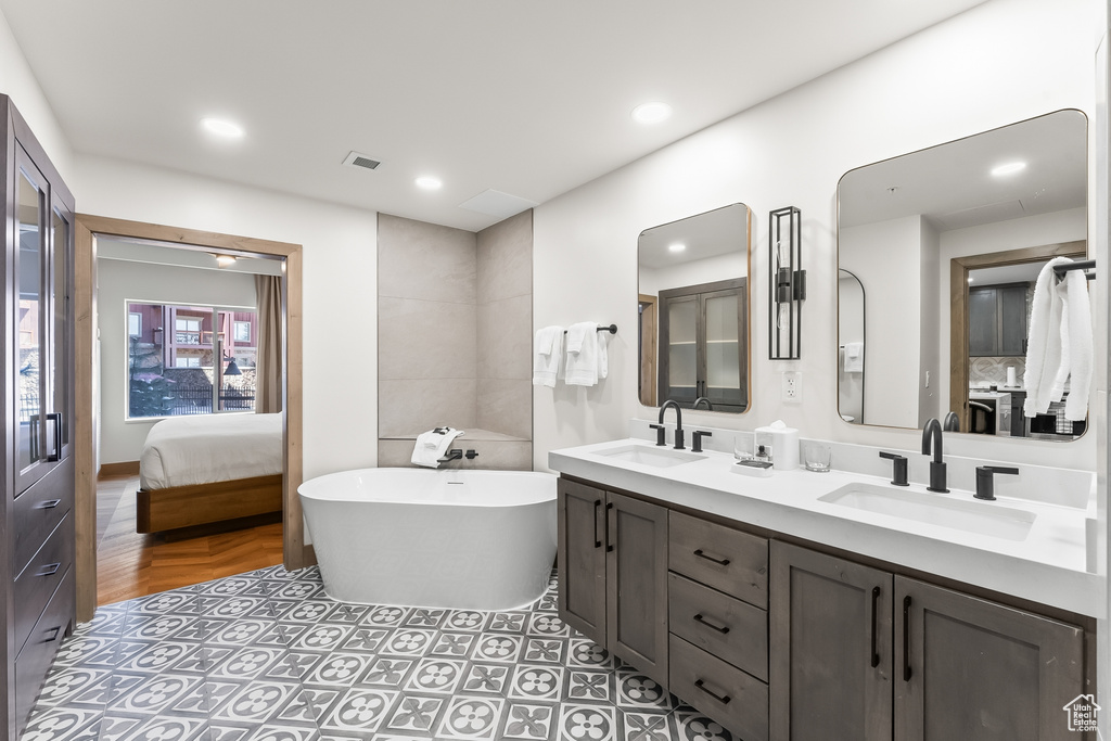 Bathroom featuring a bathing tub, tile floors, vanity with extensive cabinet space, and dual sinks