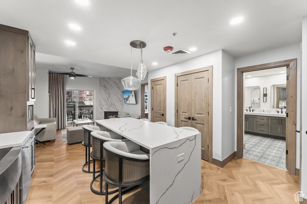 Kitchen featuring a kitchen breakfast bar, hanging light fixtures, light stone countertops, ceiling fan, and light parquet flooring