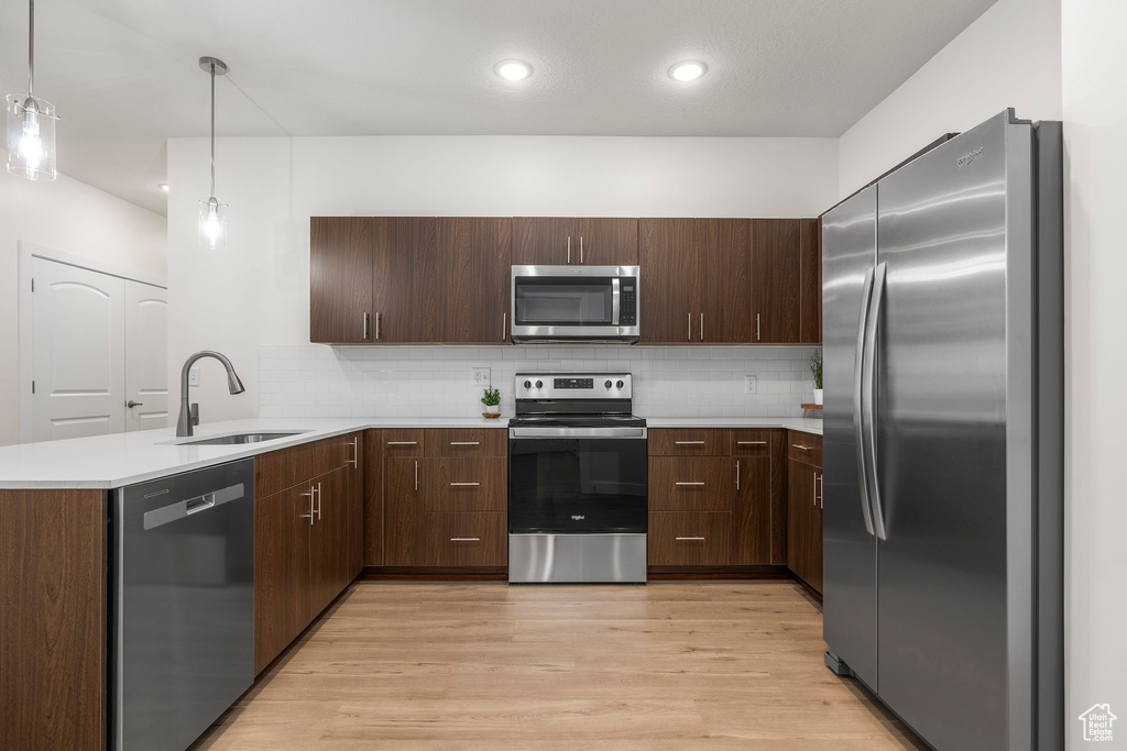 Kitchen with kitchen peninsula, light hardwood / wood-style flooring, stainless steel appliances, and decorative light fixtures