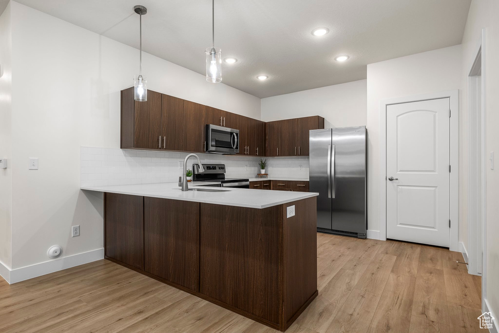 Kitchen featuring pendant lighting, light wood-type flooring, appliances with stainless steel finishes, tasteful backsplash, and kitchen peninsula