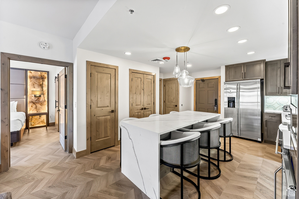 Kitchen with hanging light fixtures, high end fridge, light parquet floors, light stone counters, and a kitchen island