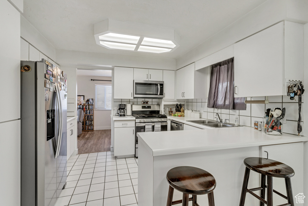 Kitchen with appliances with stainless steel finishes, a breakfast bar, white cabinets, and light tile floors