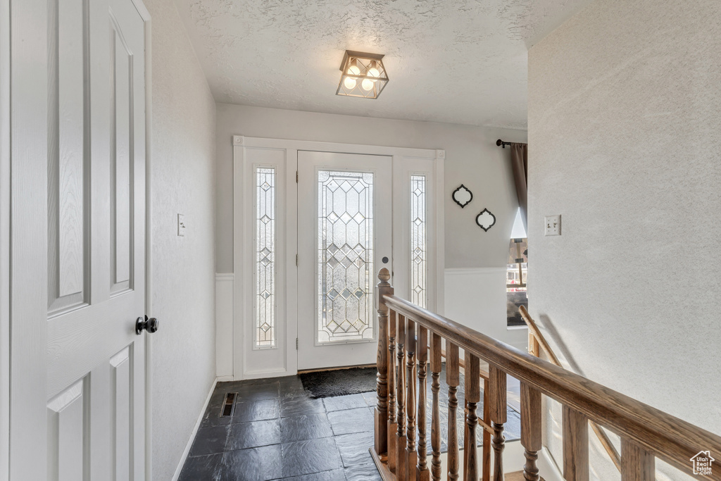 Foyer entrance featuring dark tile flooring, a wealth of natural light, and a textured ceiling