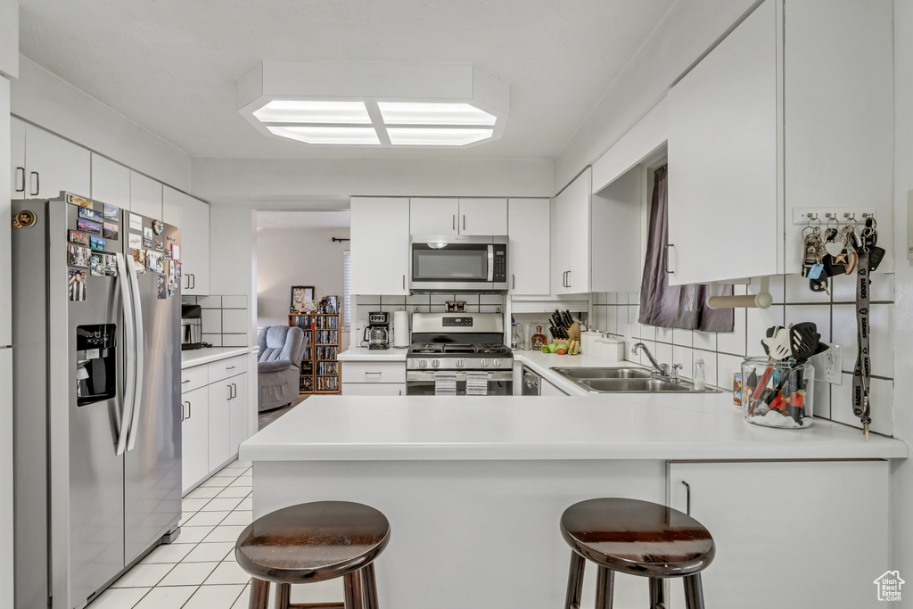 Kitchen featuring appliances with stainless steel finishes, light tile floors, a kitchen bar, sink, and white cabinetry