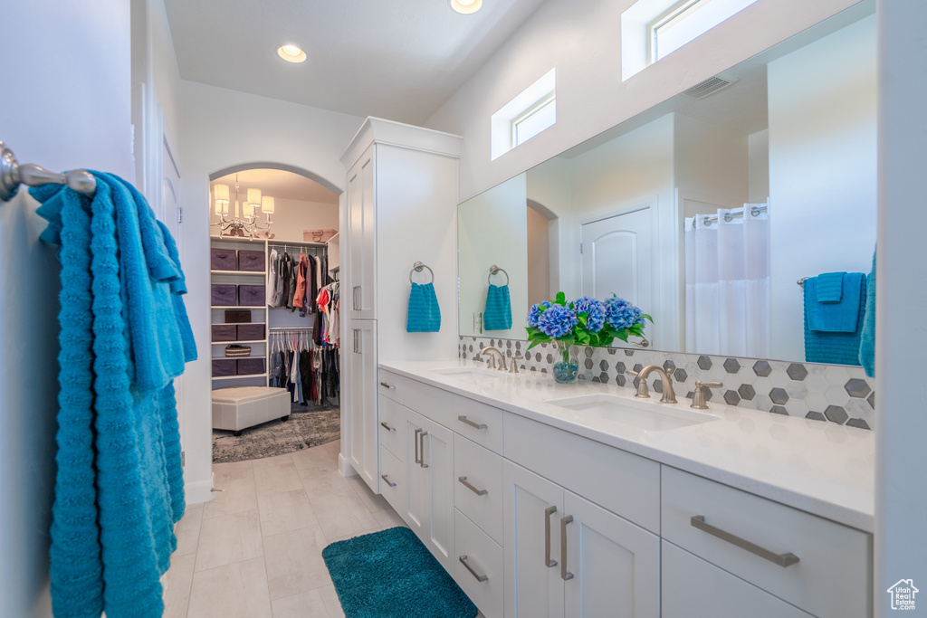 Bathroom with oversized vanity, tile flooring, tasteful backsplash, an inviting chandelier, and dual sinks
