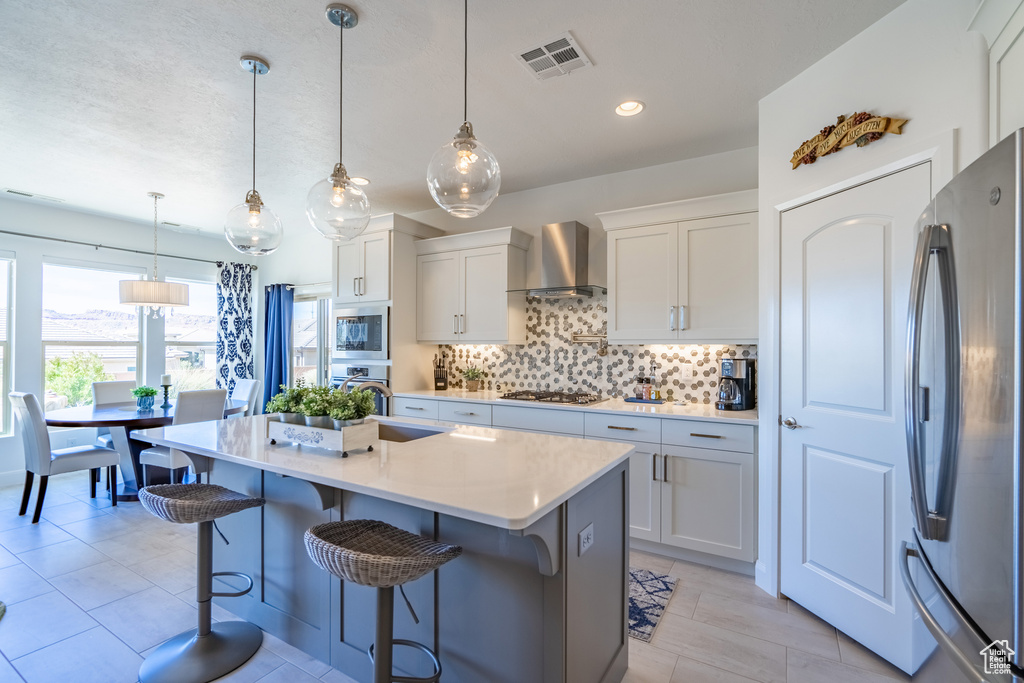 Kitchen featuring white cabinets, pendant lighting, wall chimney exhaust hood, and stainless steel appliances