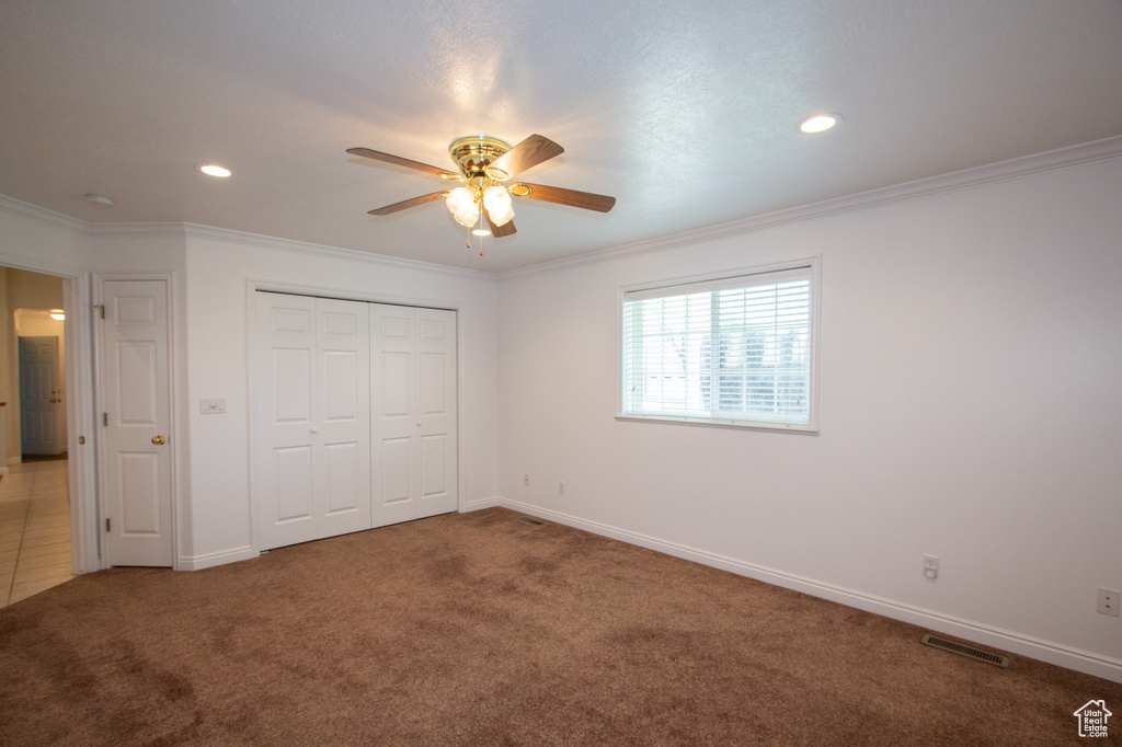Unfurnished bedroom with a closet, ceiling fan, crown molding, and dark colored carpet
