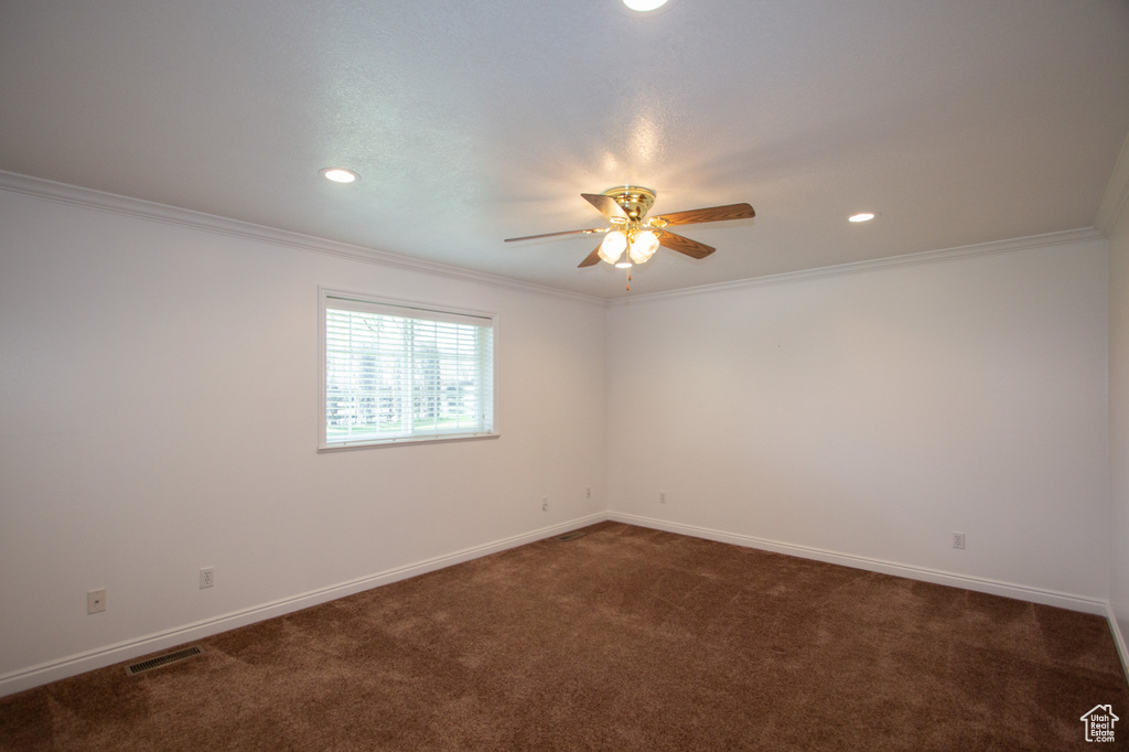 Spare room with dark colored carpet, ceiling fan, and crown molding