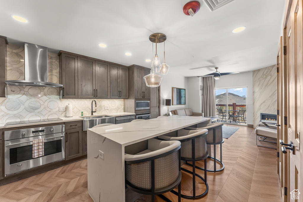 Kitchen featuring wall chimney exhaust hood, pendant lighting, light parquet floors, stainless steel appliances, and a kitchen island